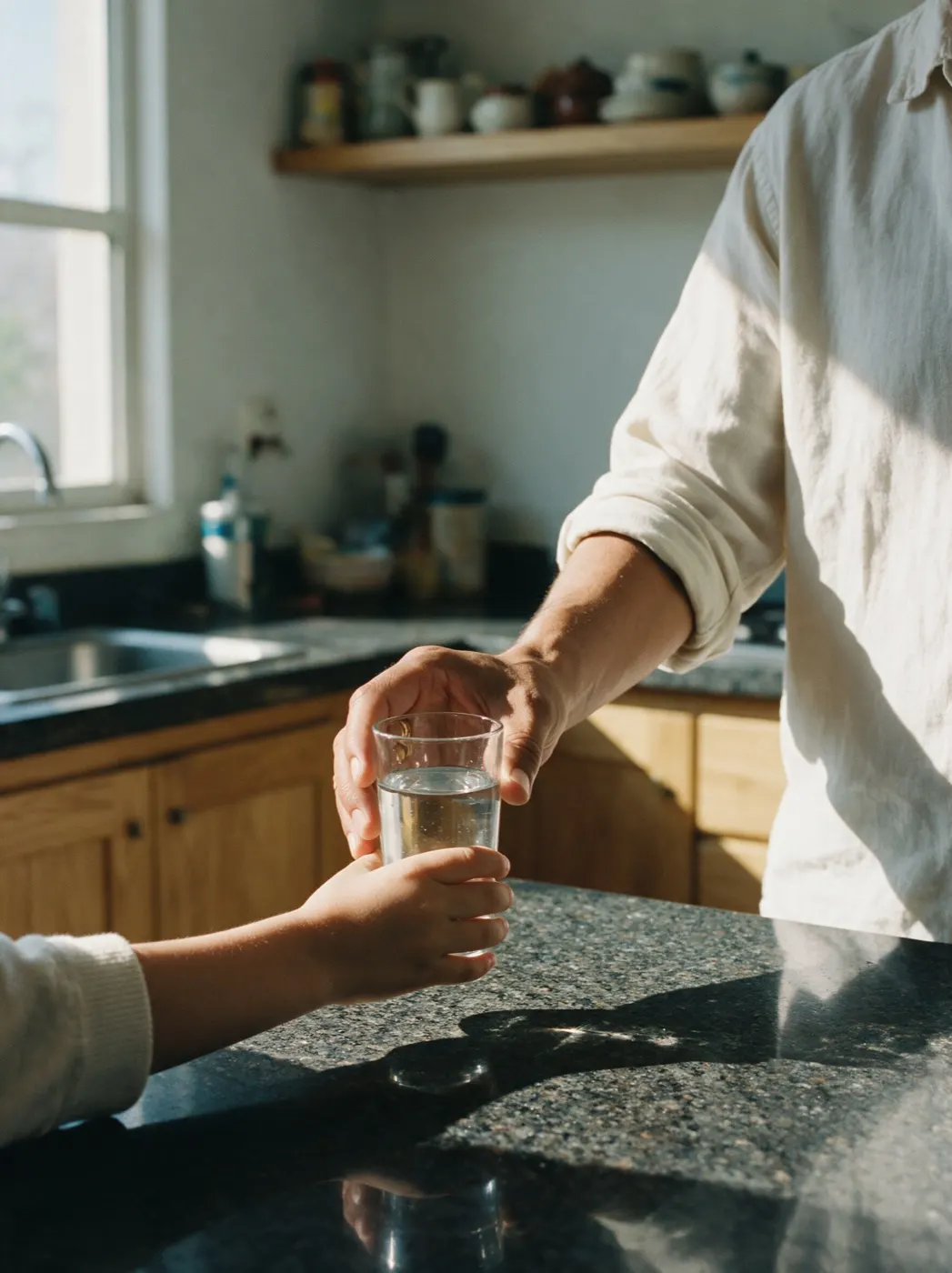 Una mano adulta pasa un vaso de agua a la mano de un niño sobre la barra