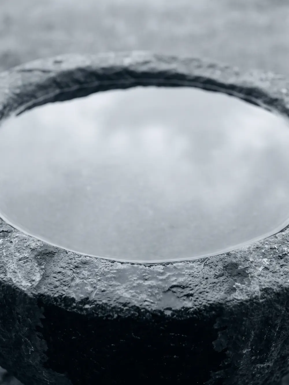Agua quieta en una pila de piedra poco profunda, reflejando un cielo gris